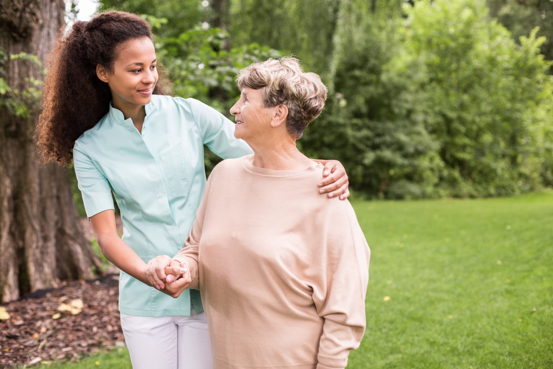 Caregiver walking outdoors hand in hand with a smiling senior woman