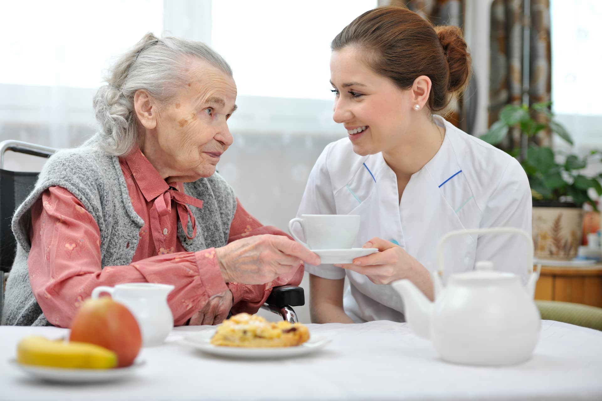 Caregiver serving tea and a homemade meal to a senior woman at her table